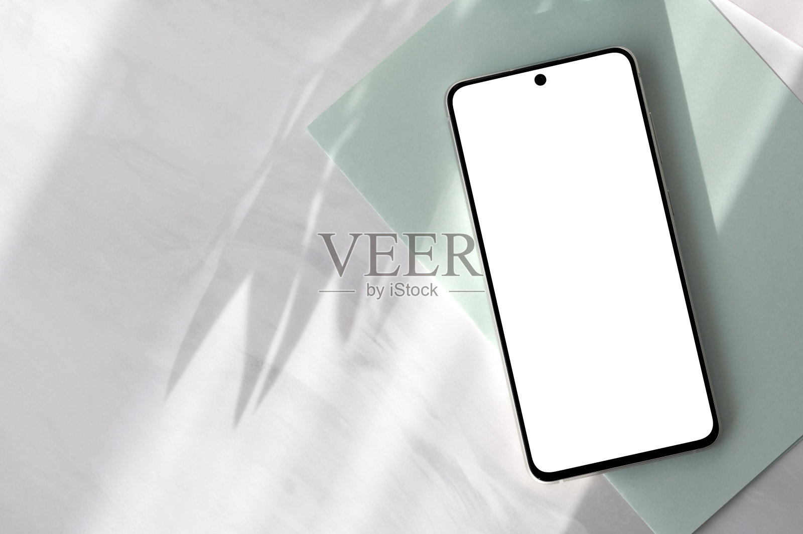 智能手机与空白屏幕模型在柔和的鼠尾绿纸和中性灰色大理石桌面背景与美学花卉自然阳光光影,优雅的春天商业品牌模板照片摄影图片