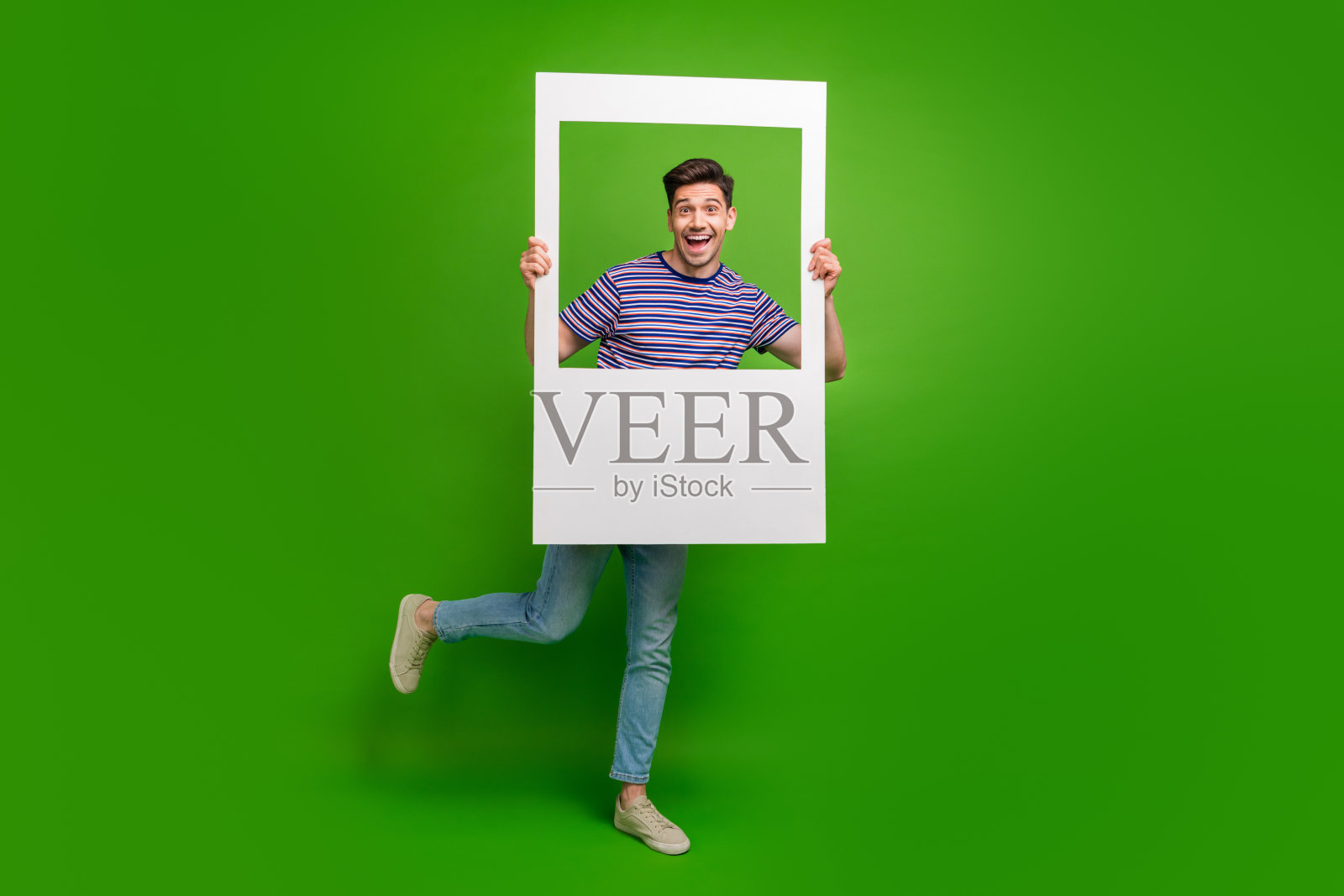 全尺寸照片欣喜若狂的家伙穿着牛仔裤条纹衬衫微笑在相框孤立的绿色背景照片摄影图片