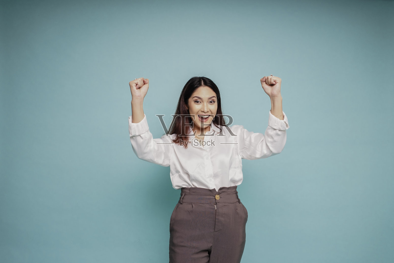 一个年轻的亚洲女人,穿着白色的衬衫,蓝色的背景衬托出她快乐成功的表情照片摄影图片