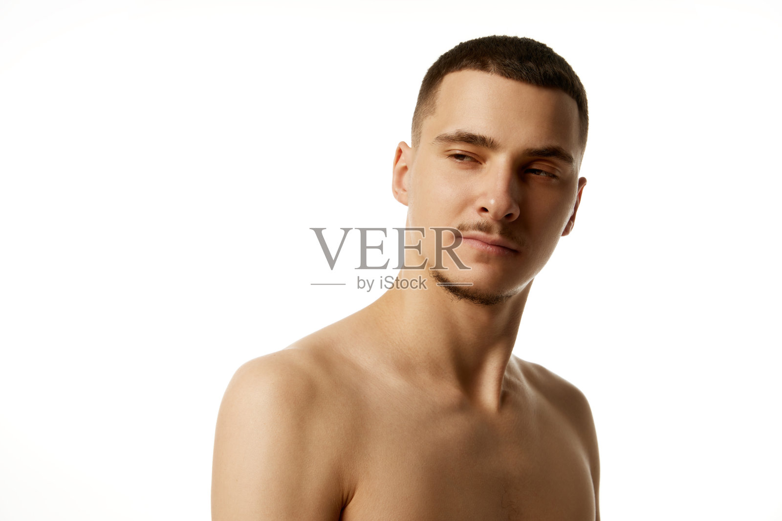 赤裸上身的年轻英俊男子,留着短发和胡子,在白色的工作室背景下微微傻笑。照片摄影图片
