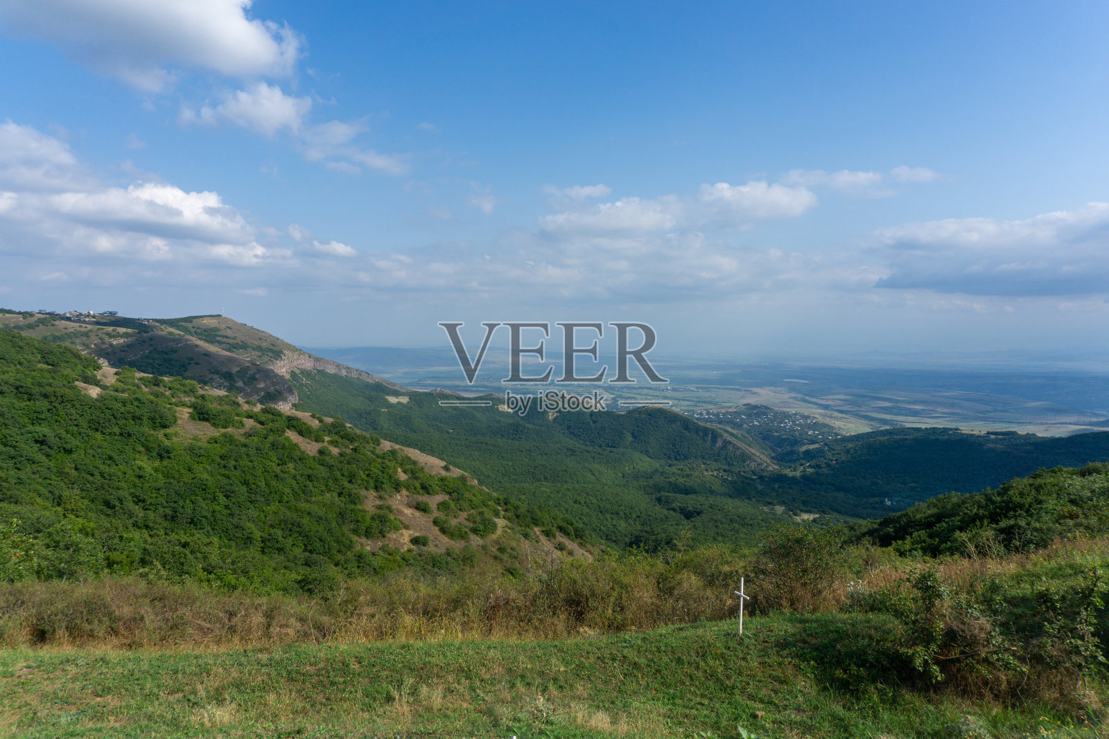 岩石和山脉的景观。明亮的蓝天和白云。前景是绿草。附近山脉和村庄的景色。格鲁吉亚。照片摄影图片