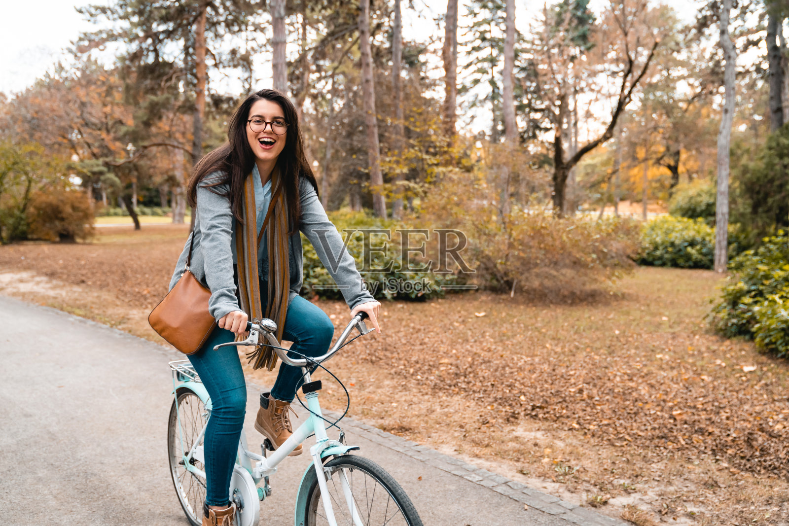 一个开朗的年轻女子,留着长长的棕色直发,骑着自行车穿过城市公园照片摄影图片