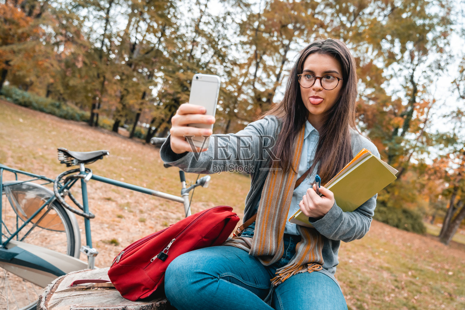 戴着眼镜的傻乎乎的年轻女人独自坐在城市公园里自拍照片摄影图片