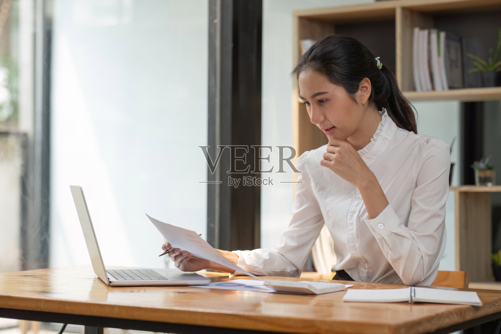 成功的亚洲女商人坐下来与数字和图表打交道。在办公室桌子上的笔记本电脑上照片摄影图片