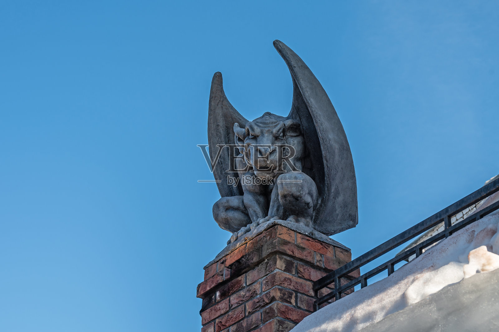 石膏石像鬼坐在屋顶上,映衬着蓝天。照片摄影图片