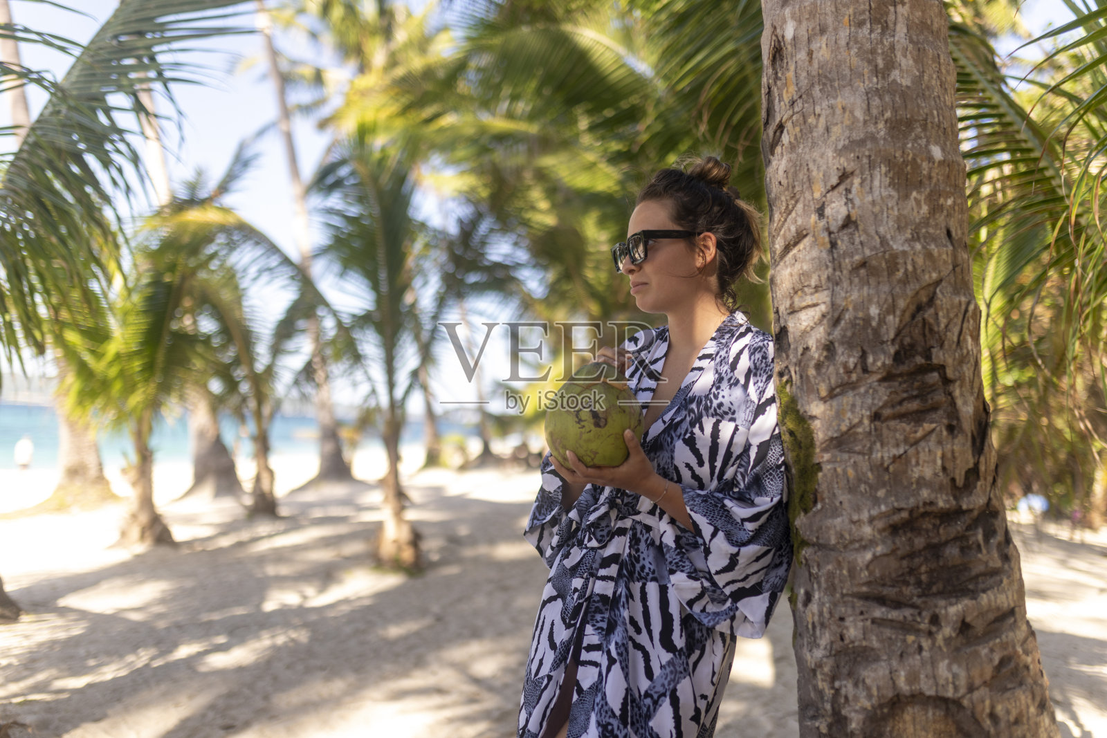 一个可爱的女人站在沙滩上,喝着鸡尾酒,享受着周围的美景照片摄影图片