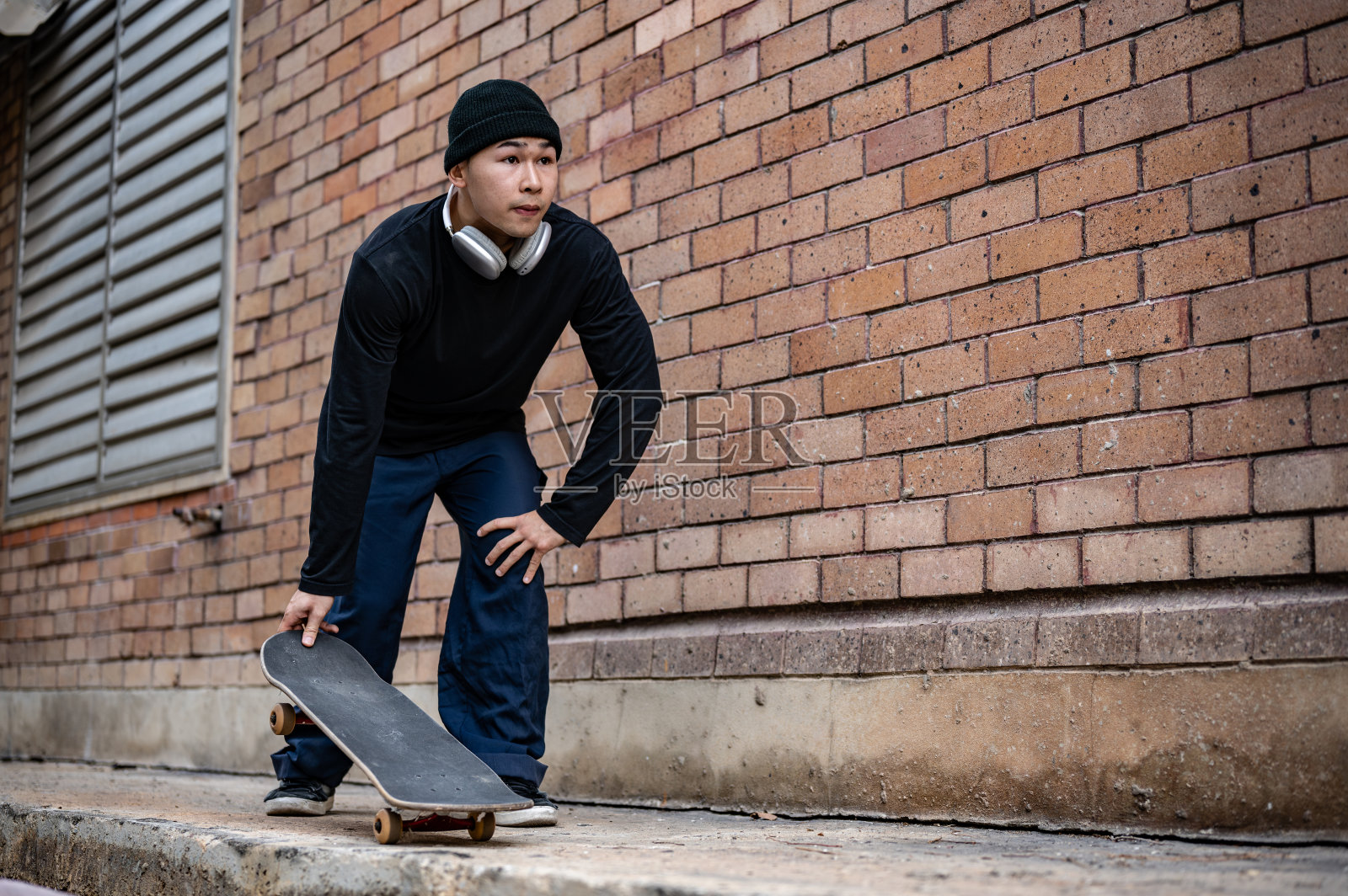 一个时尚、时髦的亚洲男性滑板手正在城市街道上练习滑板。照片摄影图片