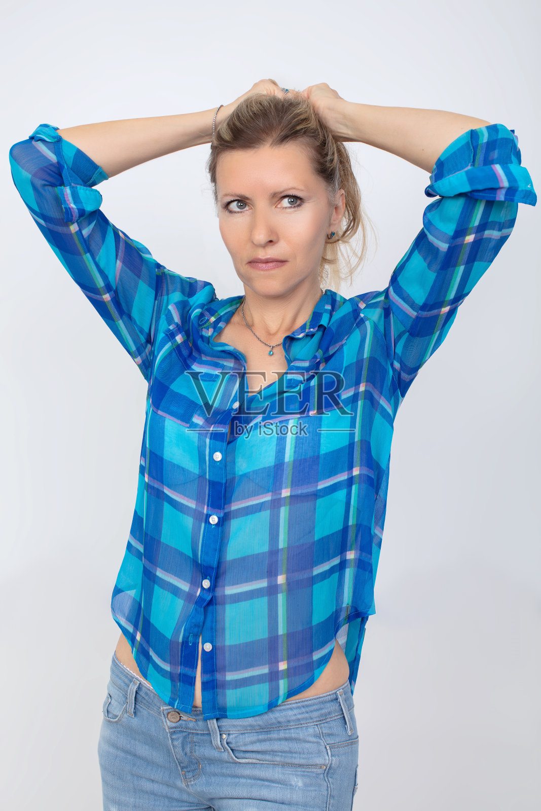 一个穿着牛仔裤和衬衫的中年妇女,背景是灰色的。照片摄影图片