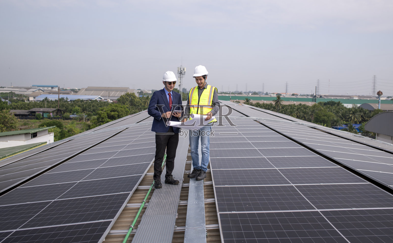 工程师走在屋顶上,拿着设备箱和无线电通讯检查太阳能电池板,太阳能电池是智能电网生态能源阳光替代发电厂的概念。照片摄影图片