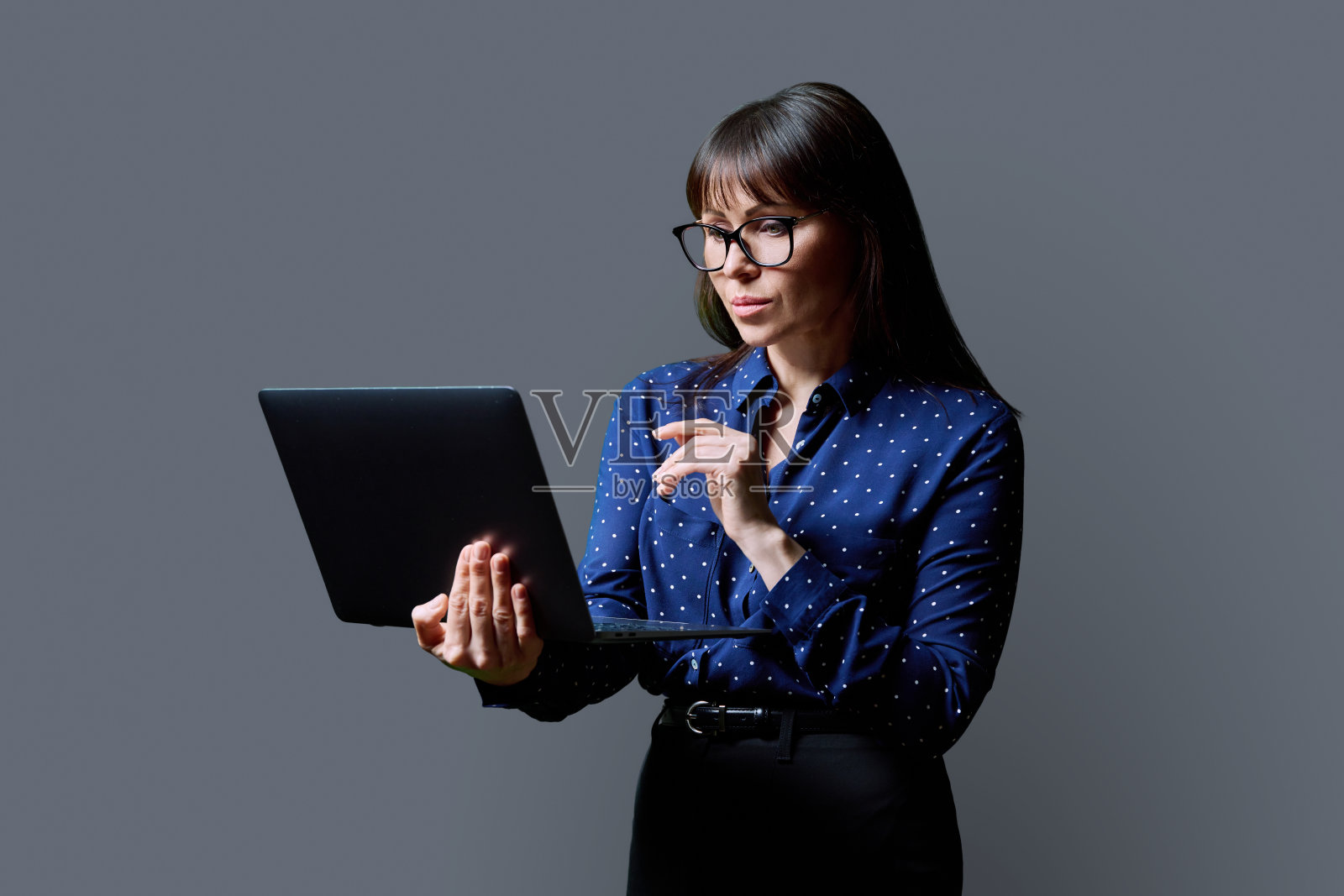 严肃的商务中年妇女使用灰色背景的笔记本电脑照片摄影图片