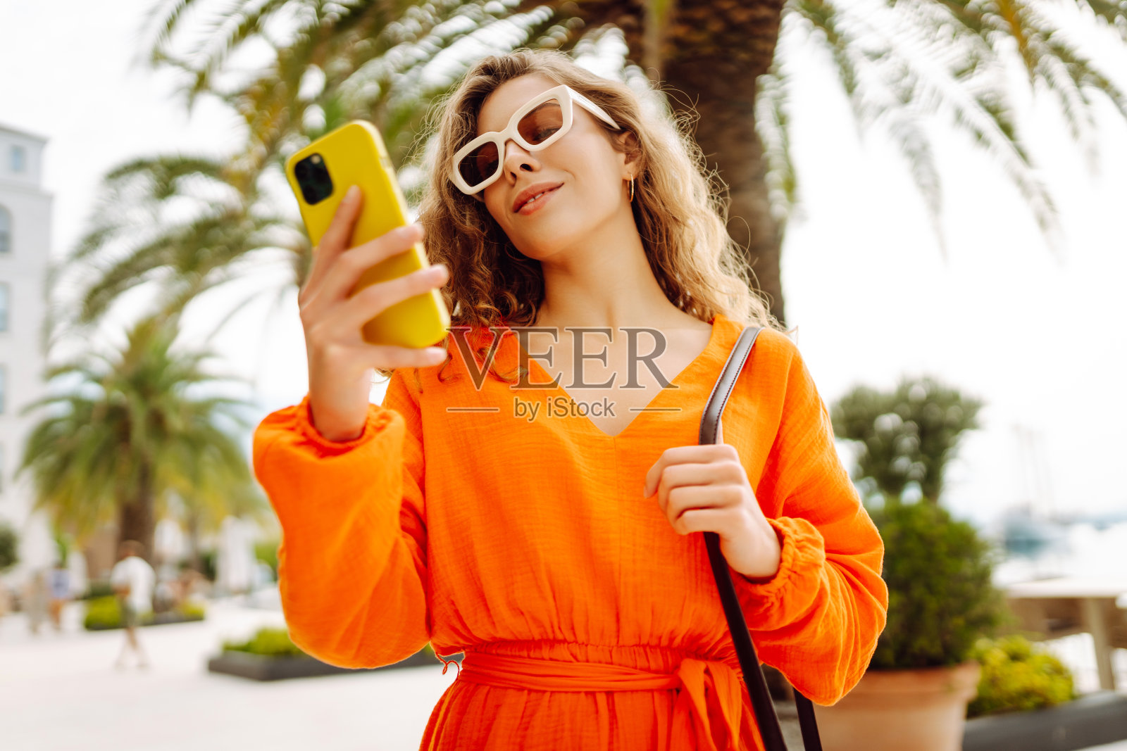 美丽的女人穿着夏装走在街上拿着手机的肖像。照片摄影图片