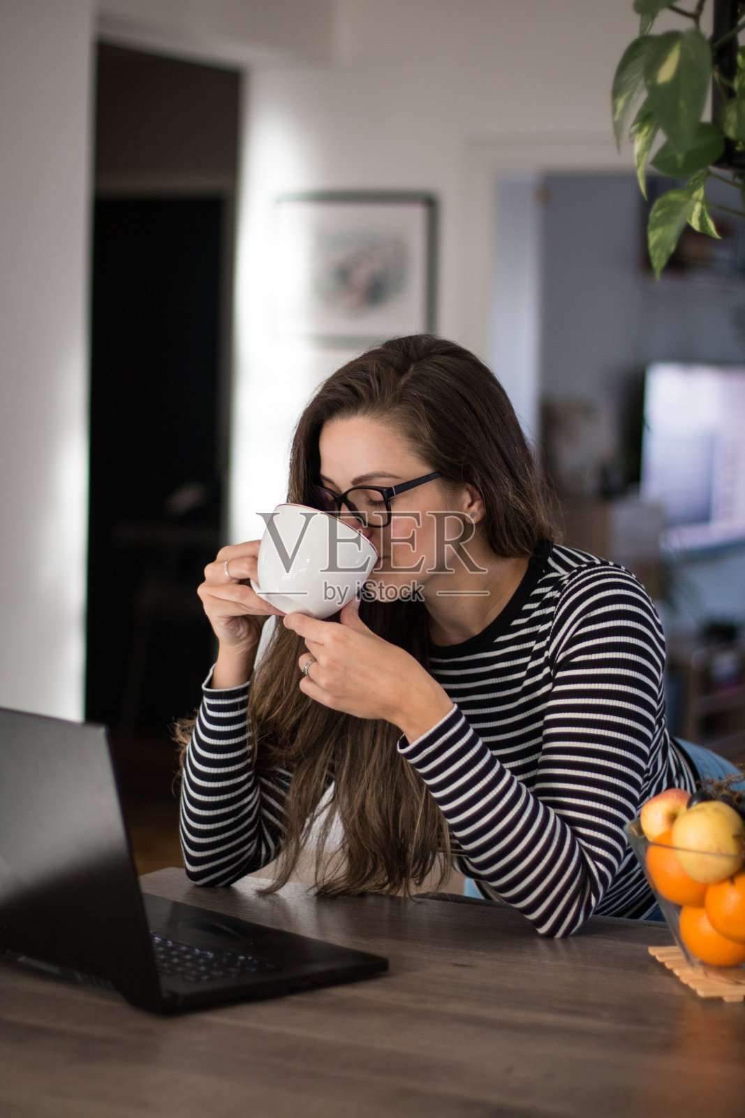 年轻女子站在餐厅里一边用笔记本电脑一边喝咖啡。照片摄影图片