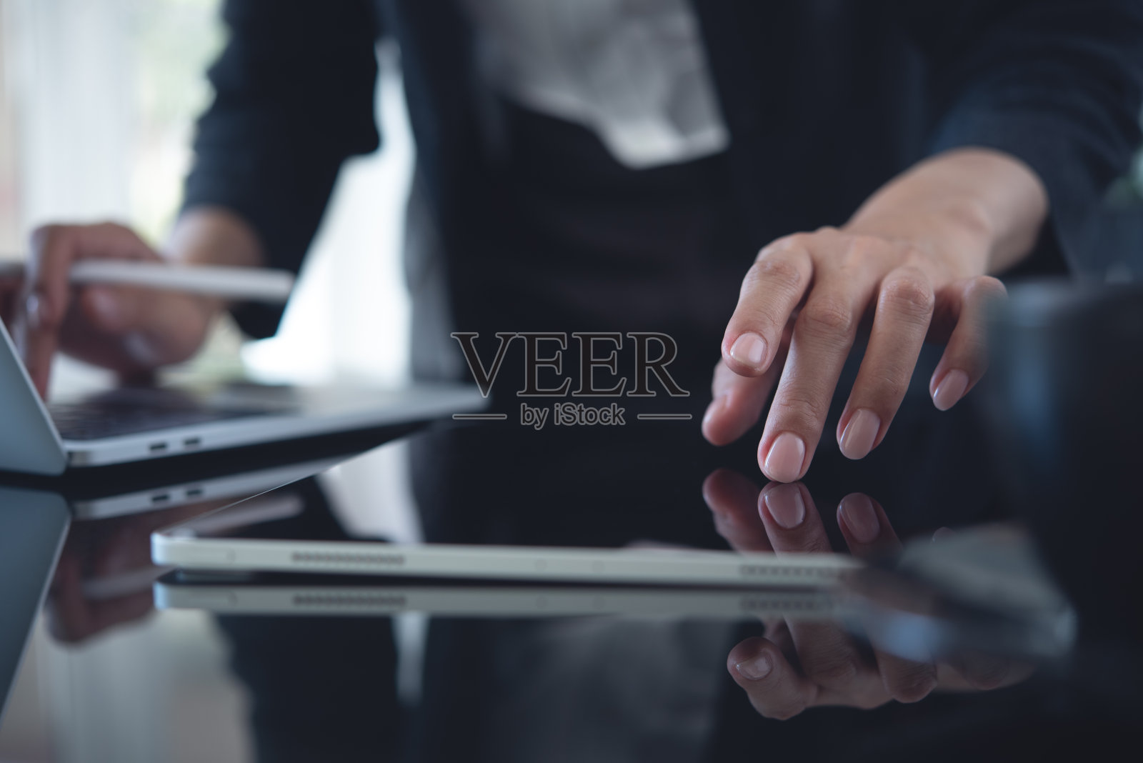 在办公室使用平板电脑和笔记本电脑的女商人。商务女性工作,触摸平板电脑屏幕,在笔记本电脑上打字,搜索商业数据,在办公桌旁上网,近距离接触照片摄影图片