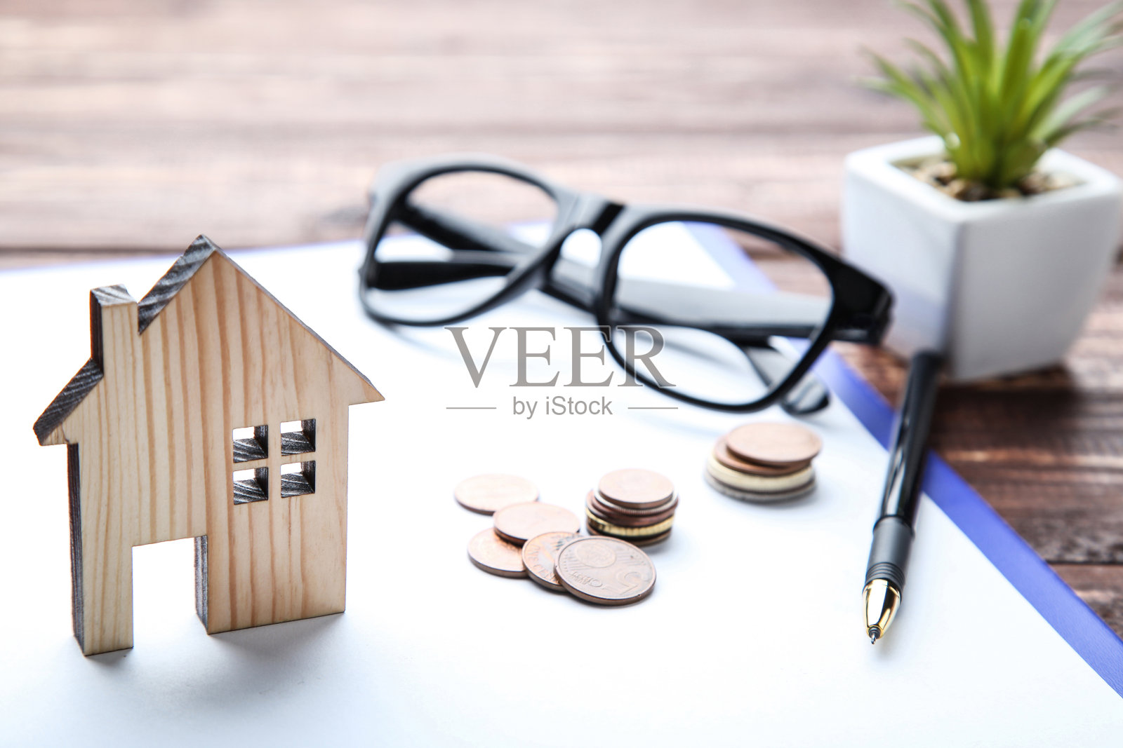 木桌上有硬币、眼镜和绿色植物的房屋模型照片摄影图片