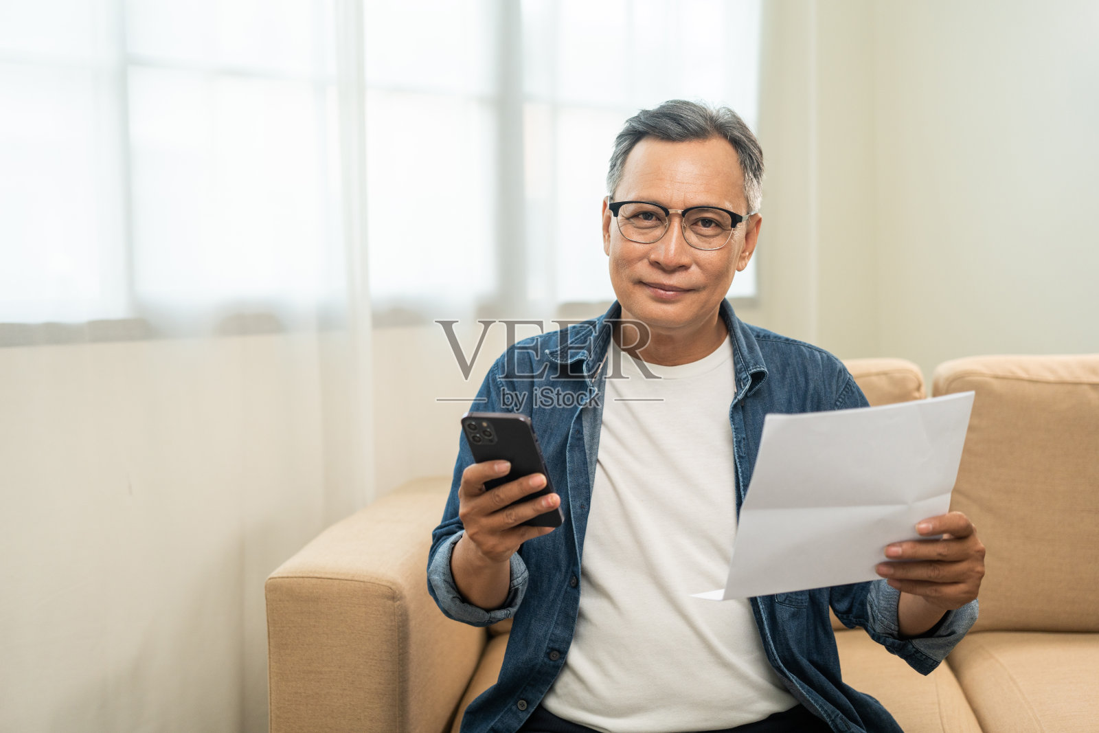 成熟的亚洲老人,有很多费用账单,用智能手机计算,用扫描二维码在线支付购买。照片摄影图片