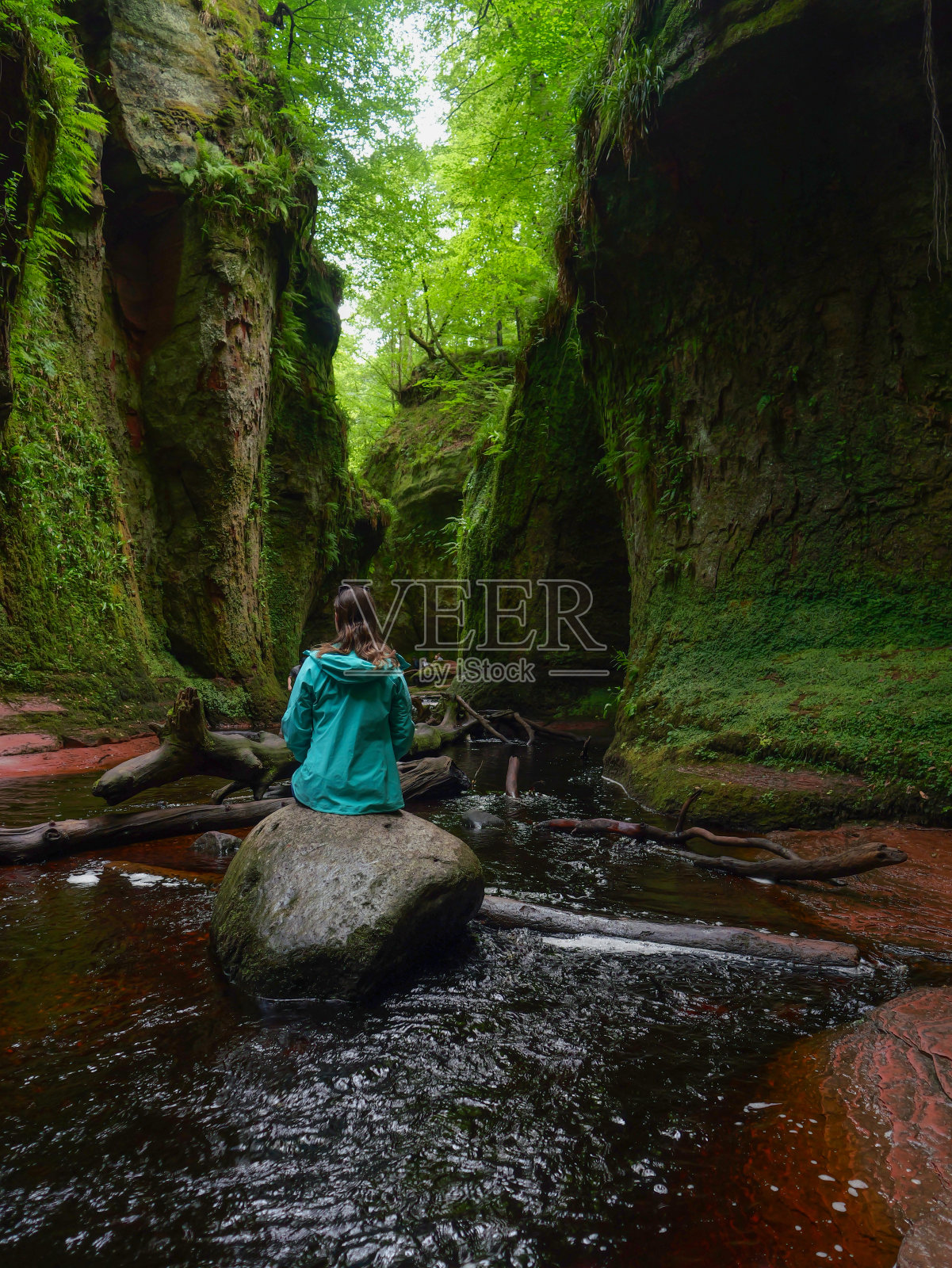 年轻女子坐在翠绿的峡谷底部的一块大石头上照片摄影图片
