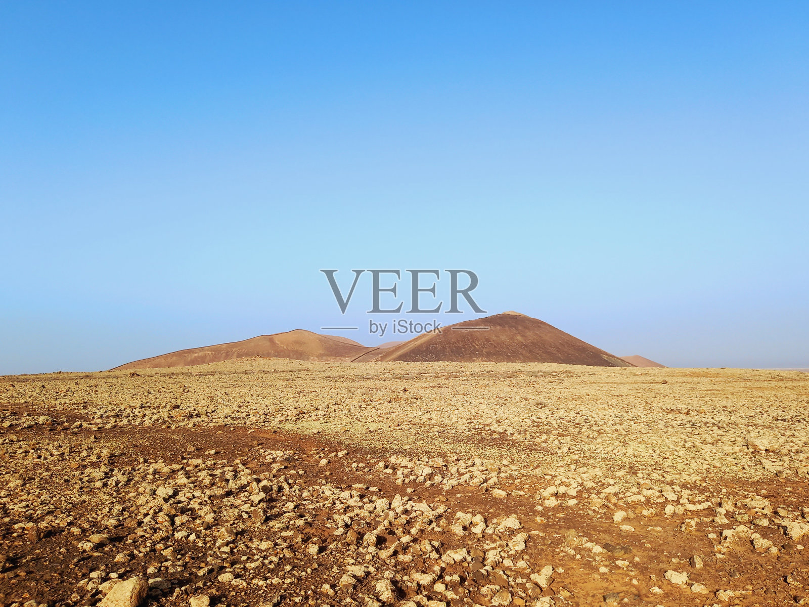 火山景观。沙漠地区有石头,岩石和砂岩和火山斜坡的剪影在蓝天下的地平线上。风景和极端的自然。照片摄影图片