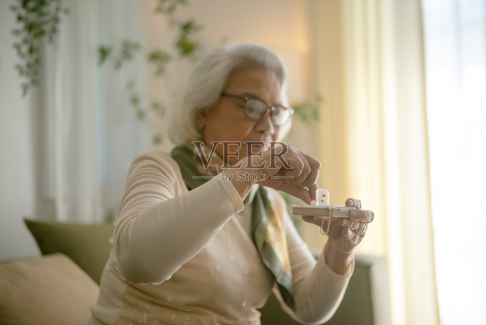 一位健康的祖母坐在客厅里看着药盒里的维生素胶囊。照片摄影图片