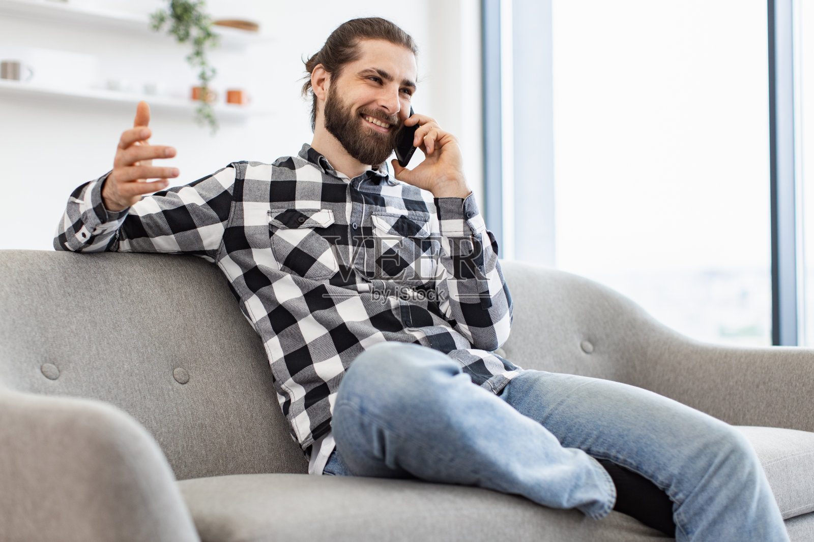 微笑的商务人士坐在沙发上,一边用手机聊天。照片摄影图片