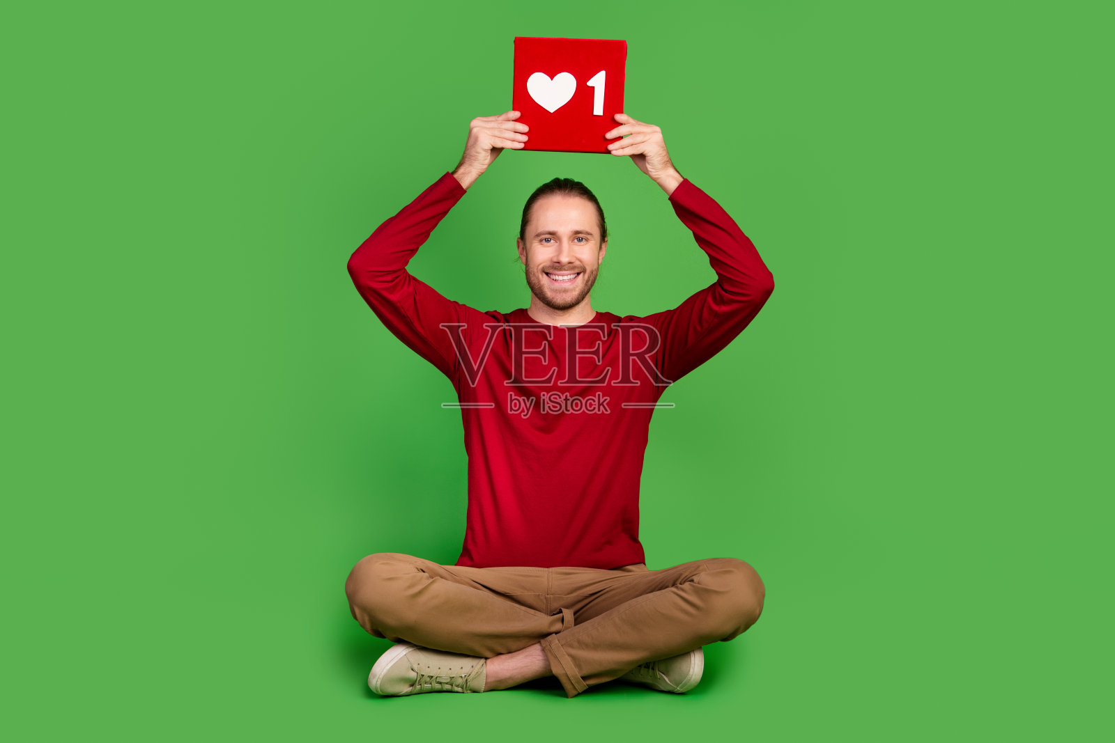 全尺寸照片好心情帅哥穿红衬衫坐在拿着红色的社交媒体像在头顶上孤立的绿色背景照片摄影图片