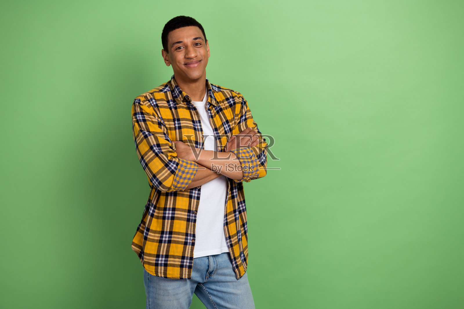 年轻迷人的大学生穿着格子衬衫,双手交叉,在他的第一份工作的地方,绿色背景孤立的照片照片摄影图片