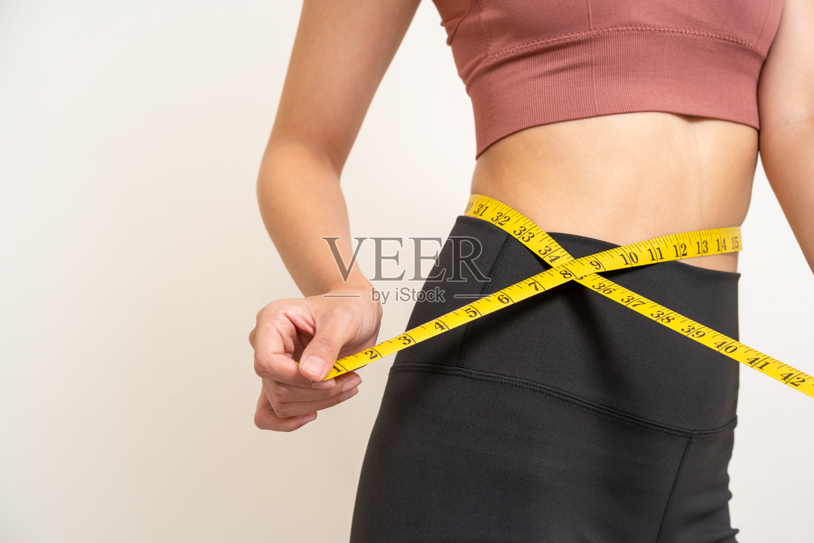 特写女人用卷尺测量她的腰围。减肥饮食疗程。穿着运动服的女人身材苗条,身材结实。注意饮食和锻炼。照片摄影图片