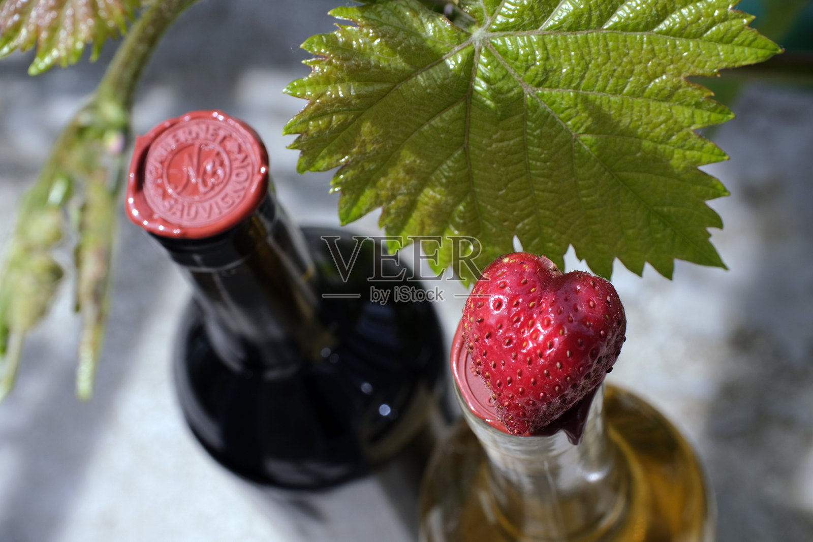 两瓶干红和干白葡萄酒,瓶口以葡萄叶为背景,配以草莓照片摄影图片