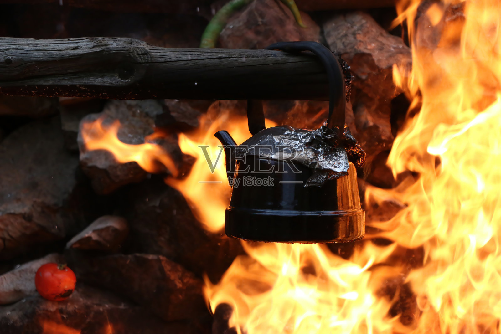一个灰色的水壶在篝火上烧着,周围有火焰。照片摄影图片