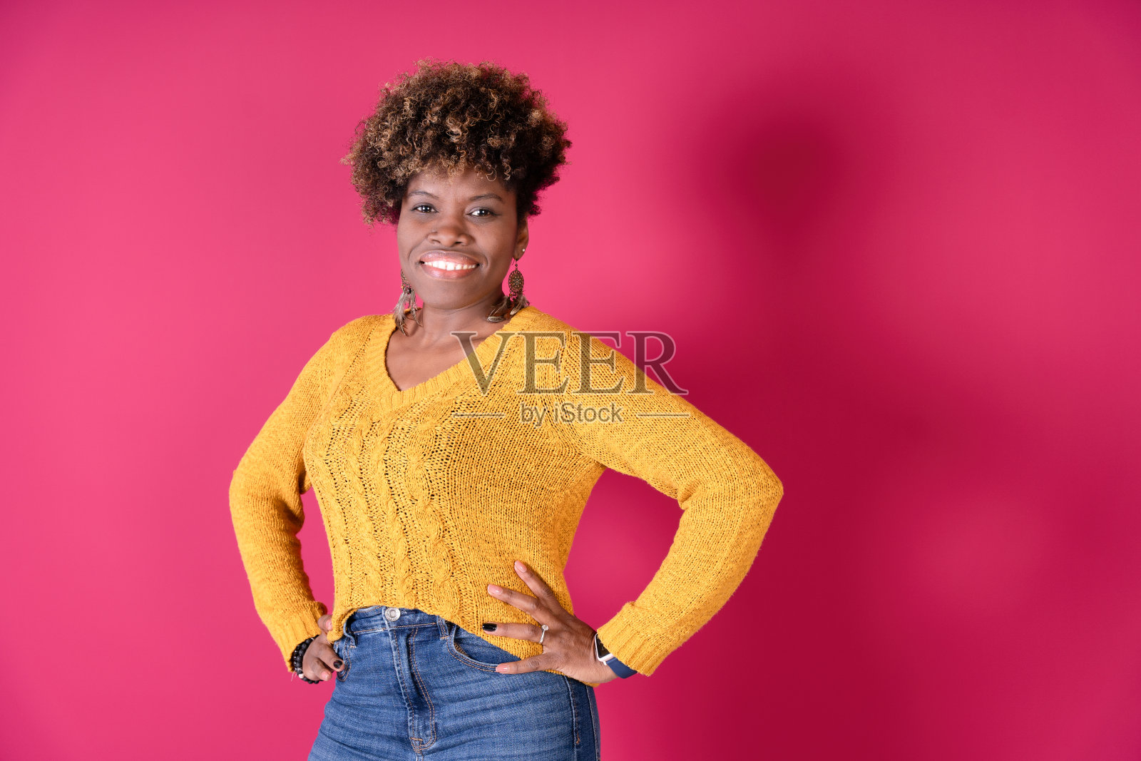 自信的年轻女子穿着黄色毛衣,在充满活力的粉红色背景下摆姿势。照片摄影图片
