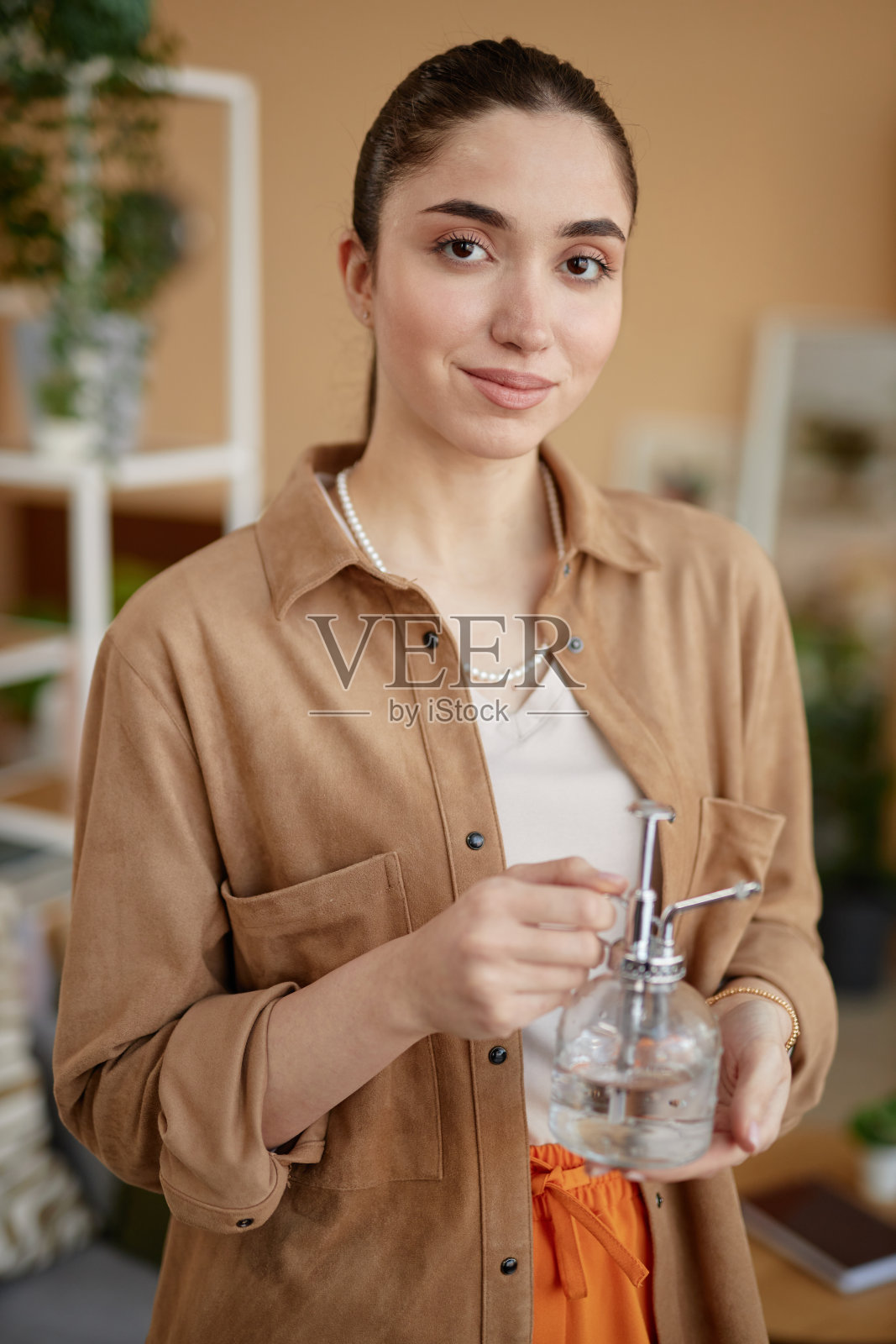 微笑的女人拿着玻璃喷壶和在家里照片摄影图片
