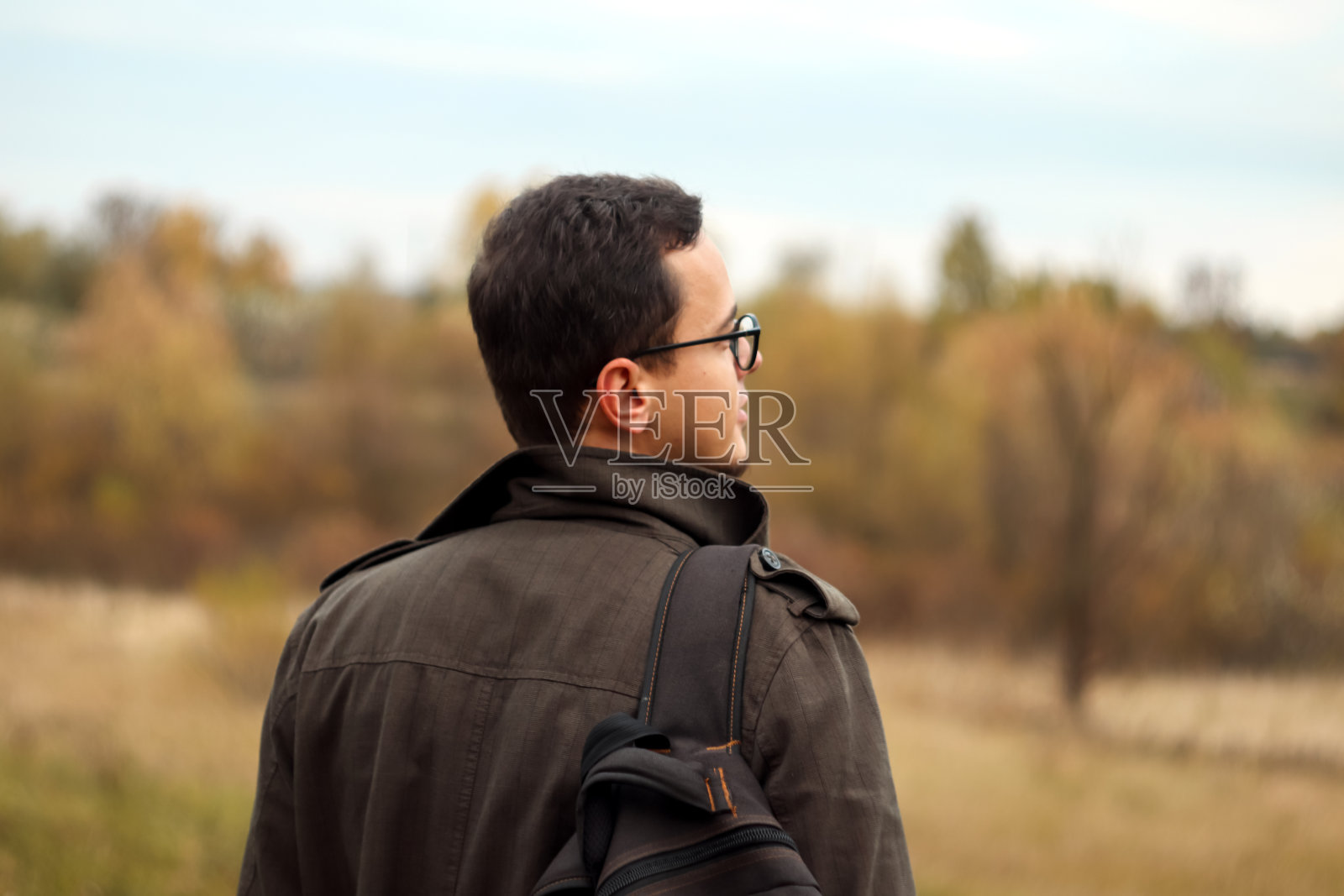 后视图游客冒险男子与背包站在秋天的自然背景。人类喜欢鼓舞人心的史诗景观。模糊照片摄影图片