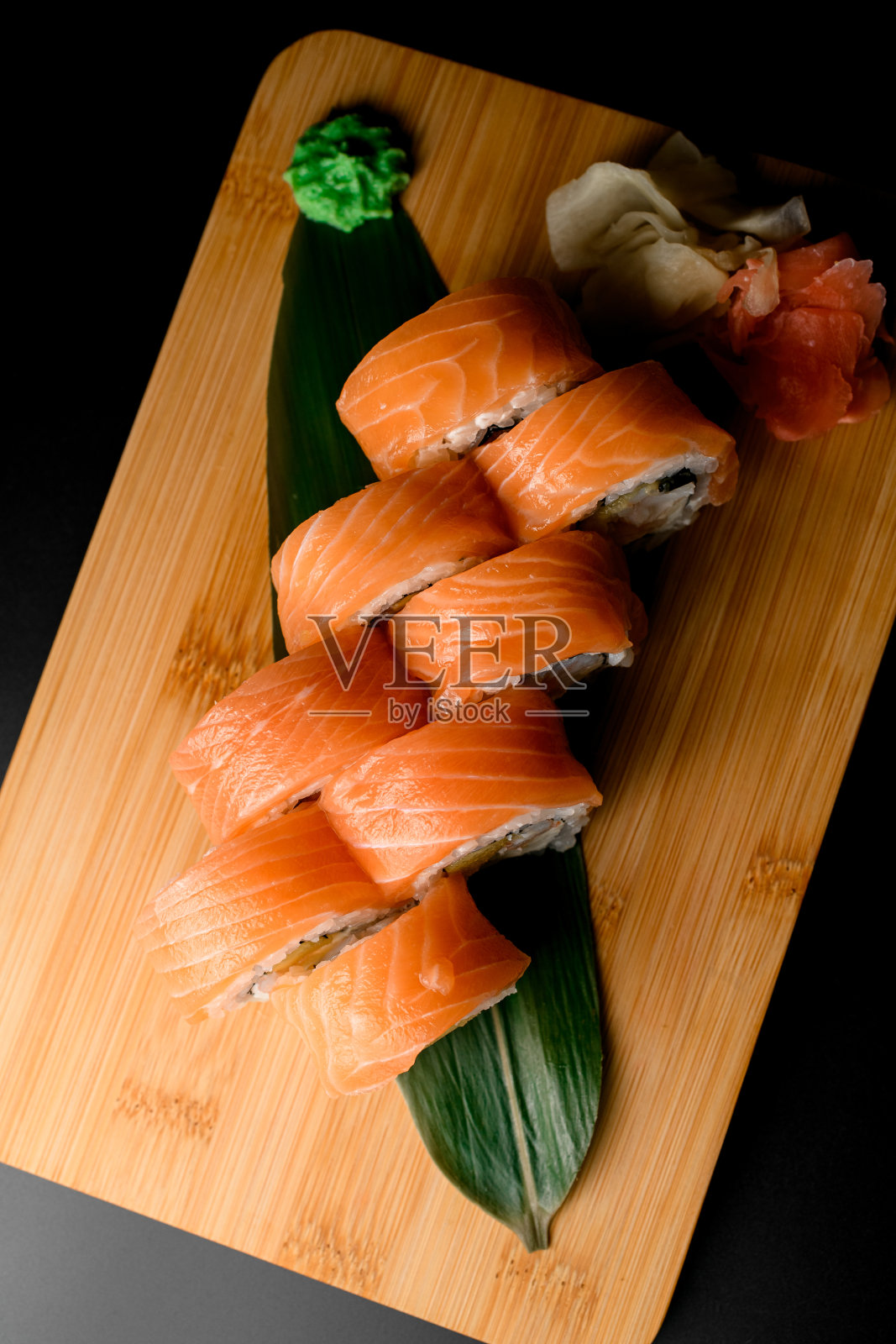 木摊上的绿叶和黑底三文鱼包的寿司照片摄影图片