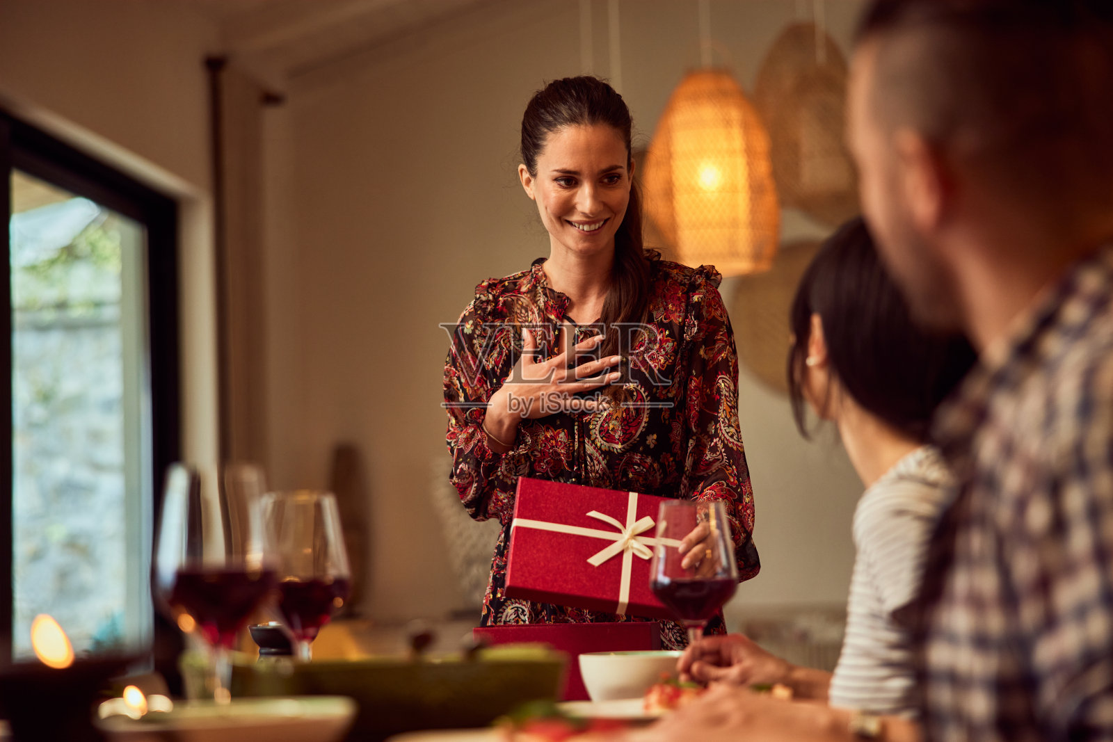 一个女人在家里吃生日晚餐,和她的朋友们一起庆祝,打开礼物。照片摄影图片