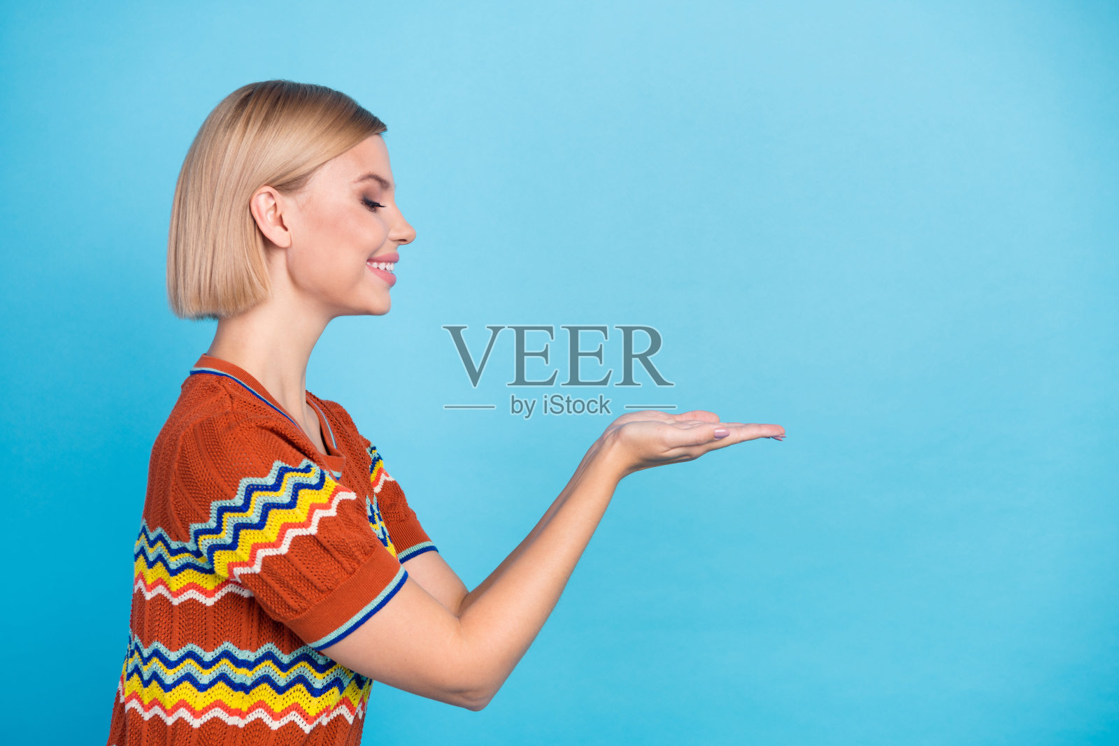 侧面肖像的华丽欣赏女人与鲍勃发型看对象在手掌上的空白空间孤立的蓝色背景照片摄影图片