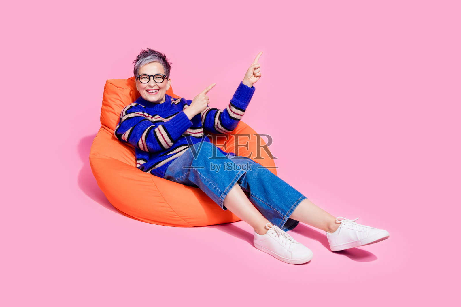 有吸引力的退休妇女的全身照片豆袋点空空间穿时髦的蓝色条纹衣服孤立在粉红色的背景照片摄影图片