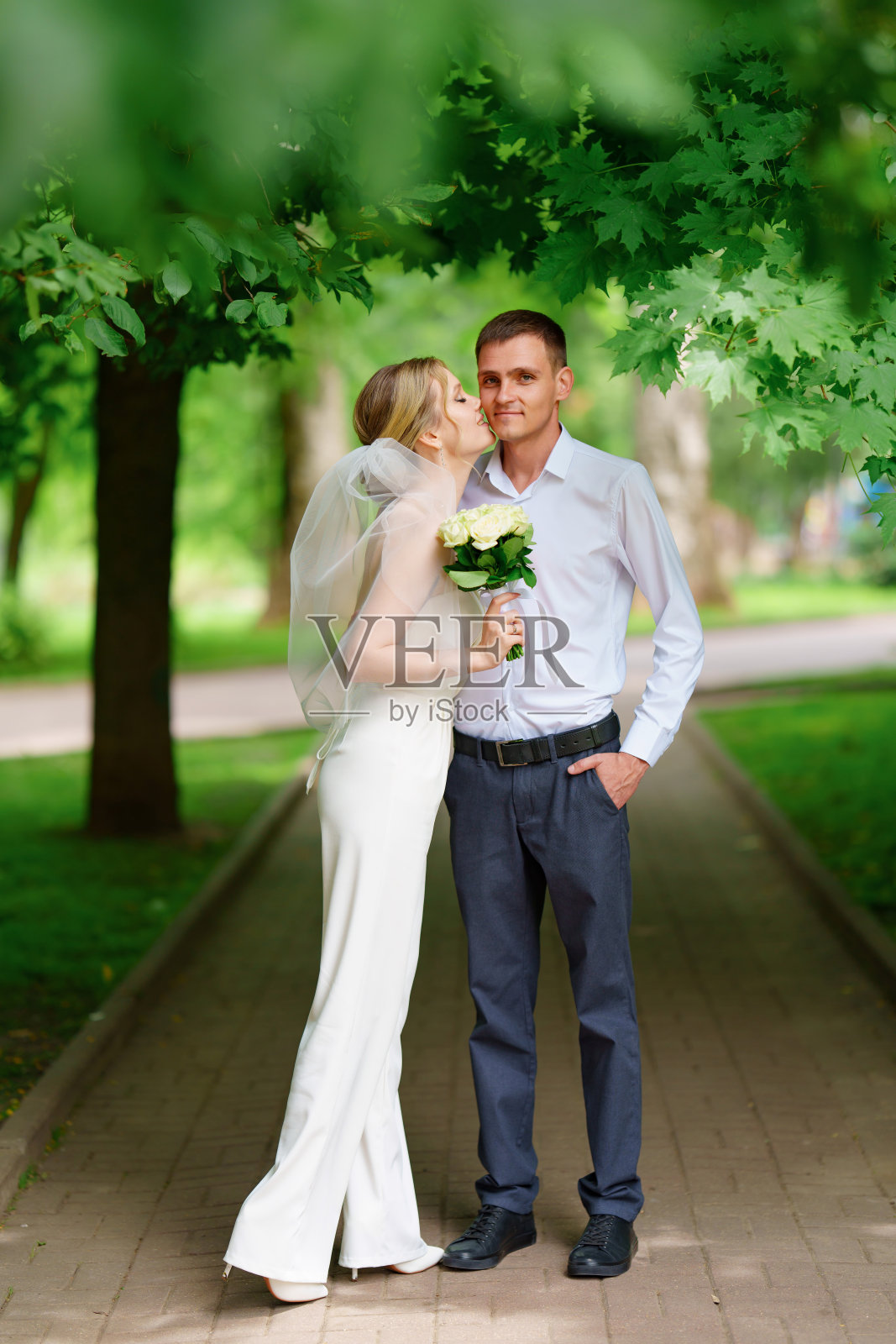 公园里幸福的一对新婚夫妇。新娘穿着裤子,戴着面纱。照片摄影图片