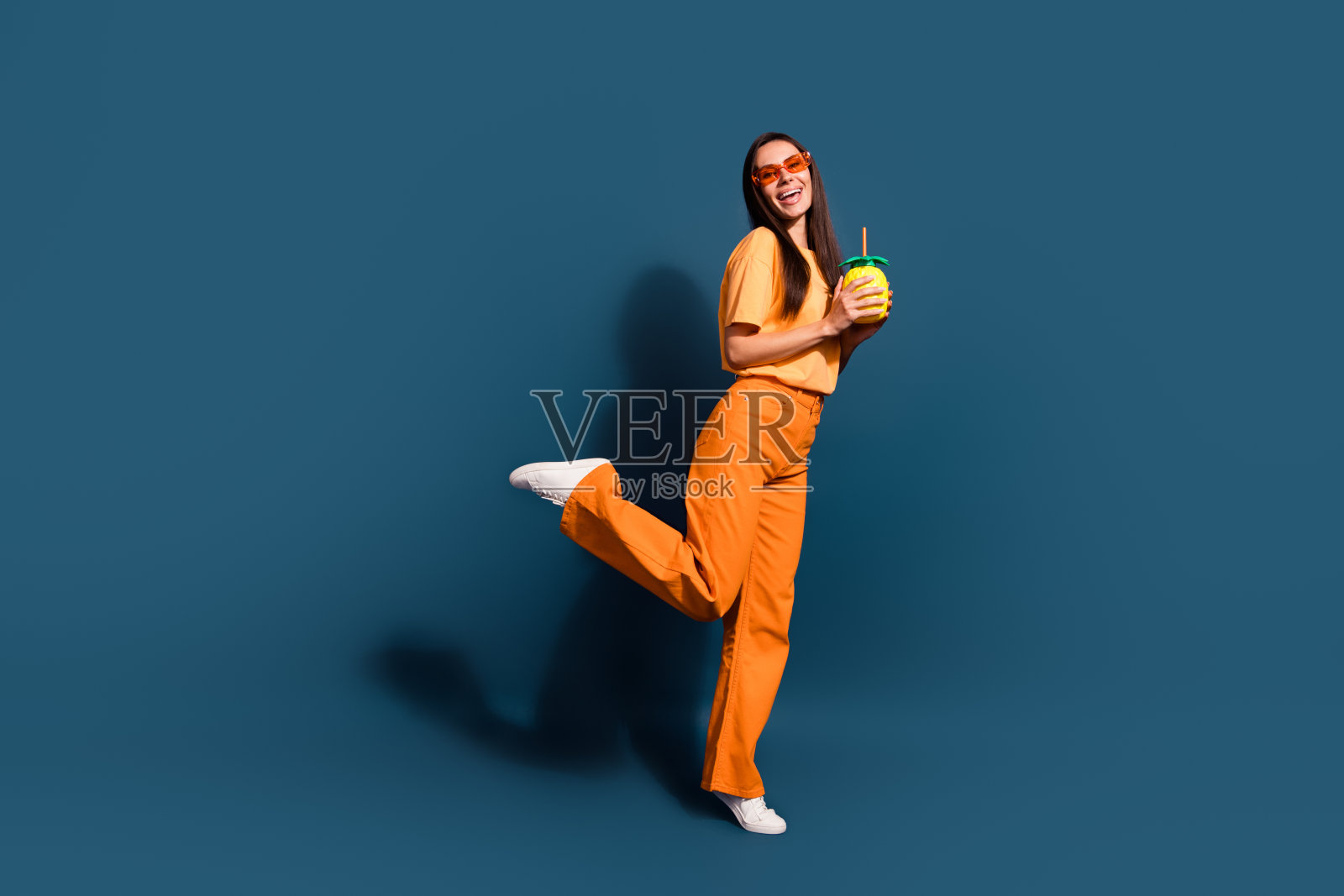 穿着黄色t恤跳舞的快乐女子在夏季聚会上拿着鸡尾酒,在深蓝色的背景上孤立照片摄影图片