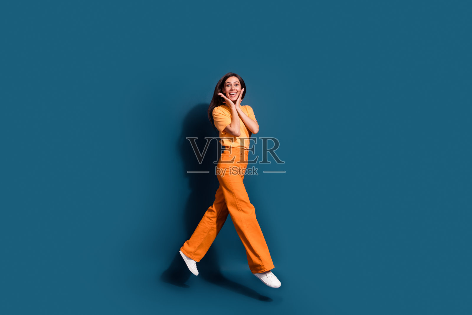 活跃的拉丁模特的全身长度的照片跳跃触摸脸颊惊讶于精品价格孤立的深蓝色背景照片摄影图片