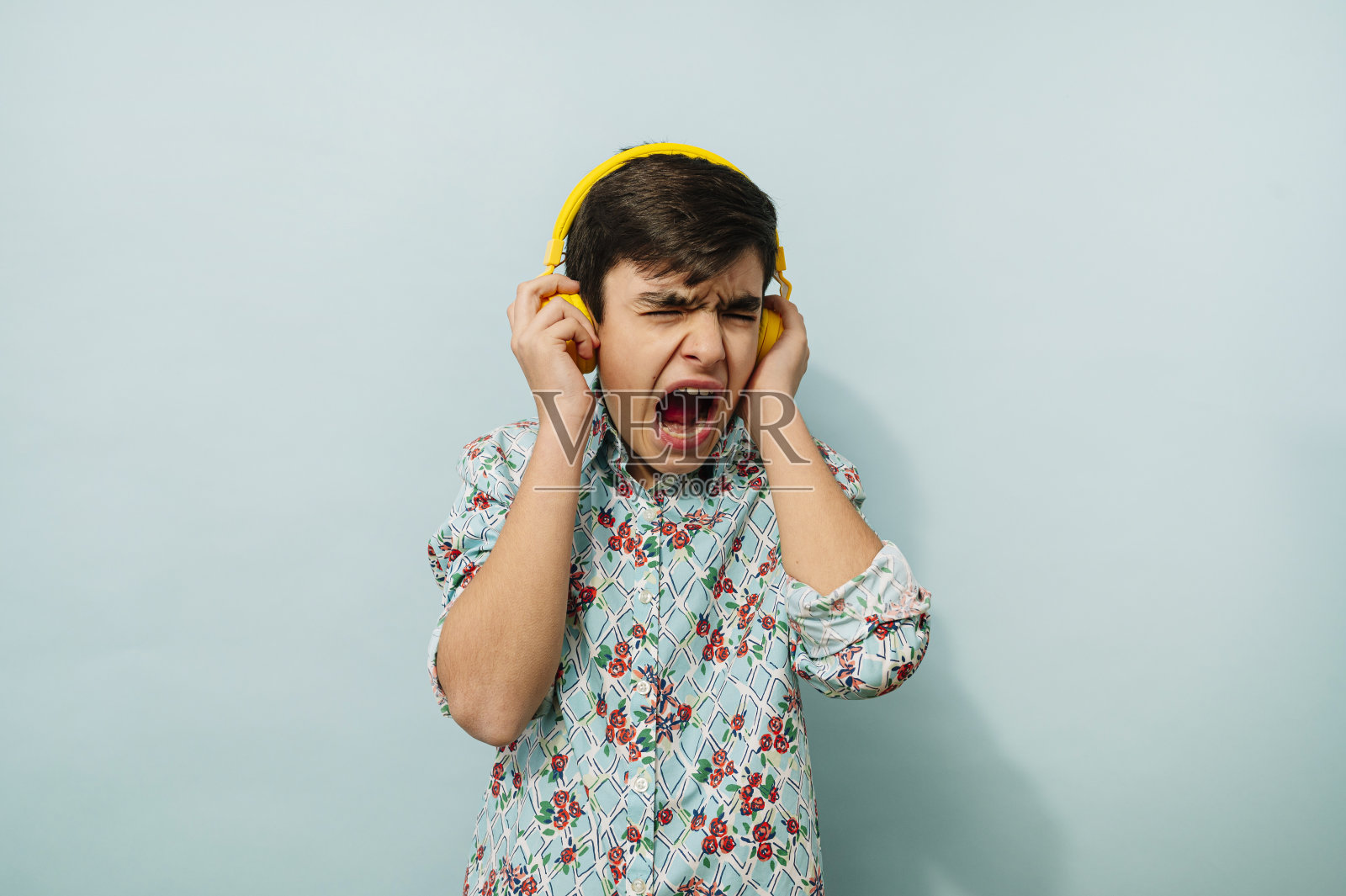 年轻人在蓝色背景的工作室里戴着黄色耳机。照片摄影图片