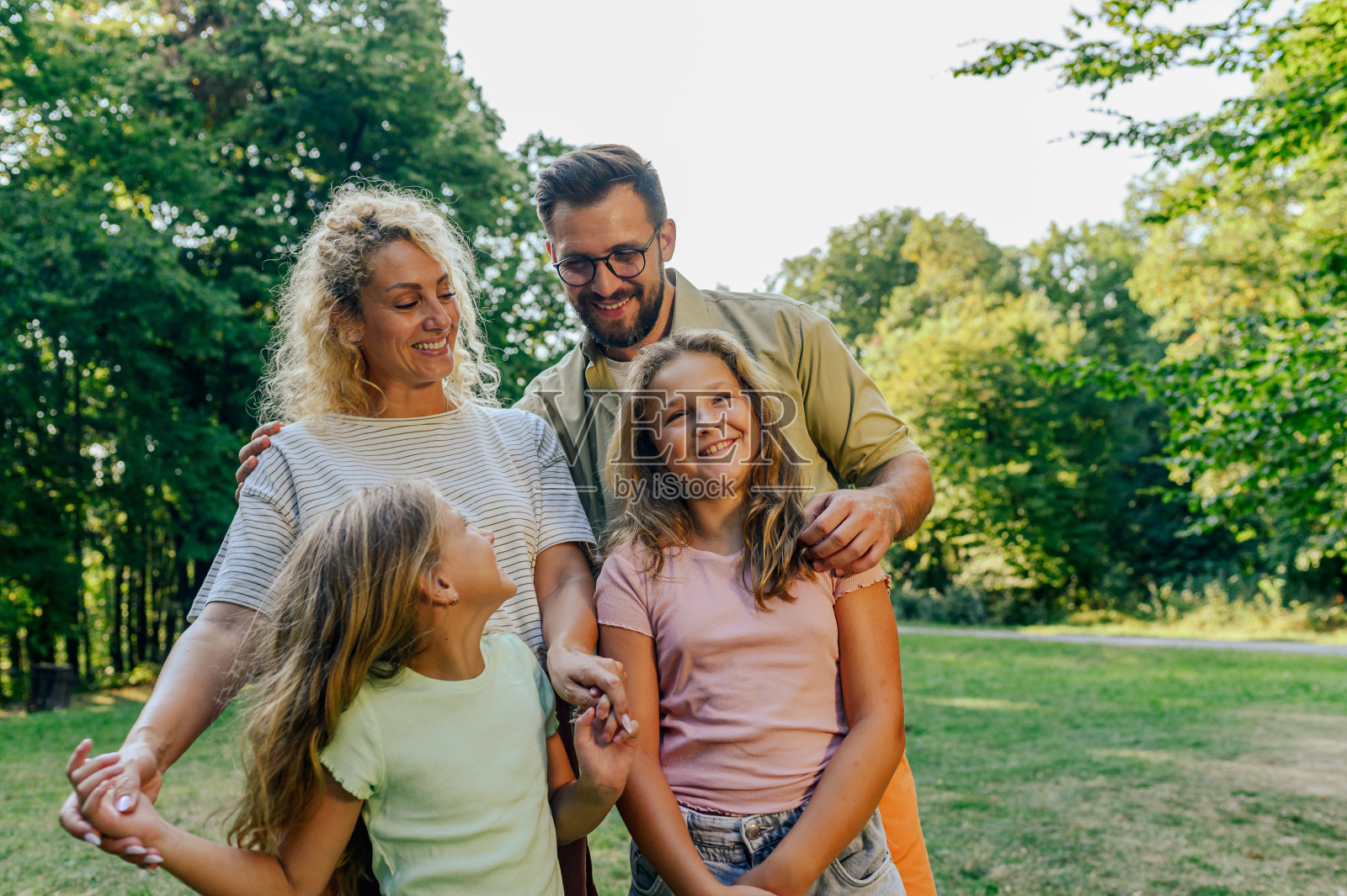 一个充满爱的四口之家站在大自然中拥抱的肖像。照片摄影图片