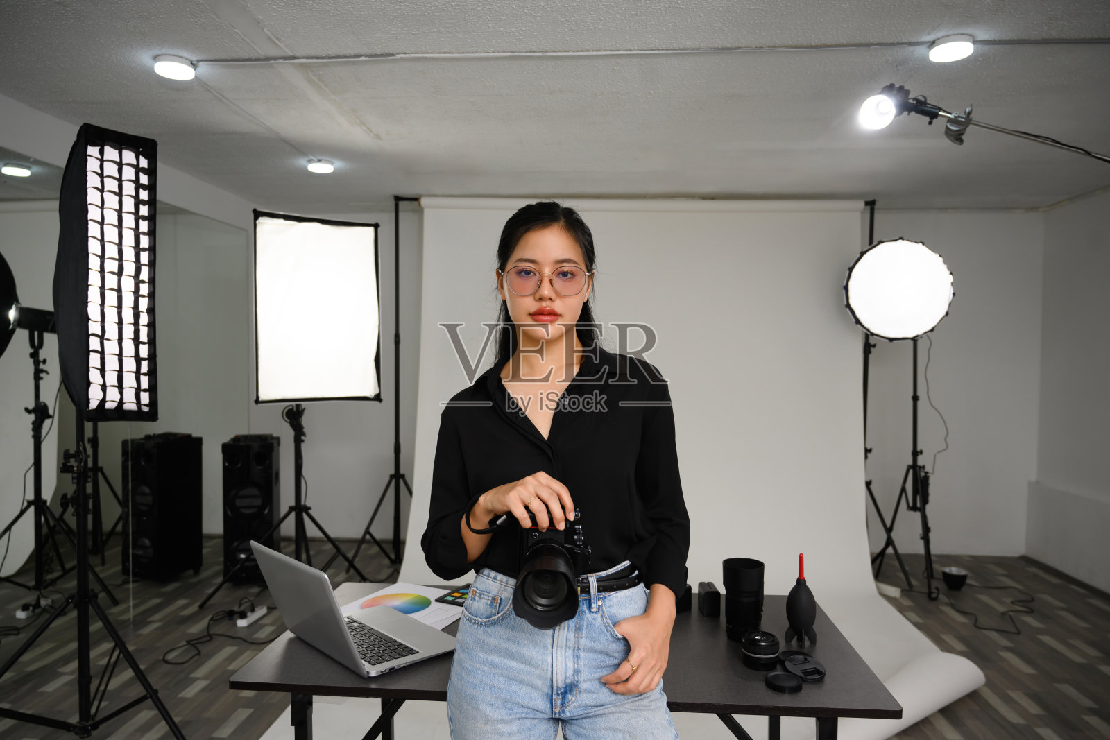 自信的女摄影师站在摄影棚与相机和照明设备的肖像照片摄影图片