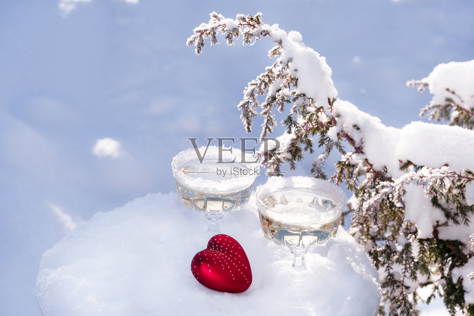 两杯起泡酒或香槟和红色的心在冬天的自然背景雪。照片摄影图片