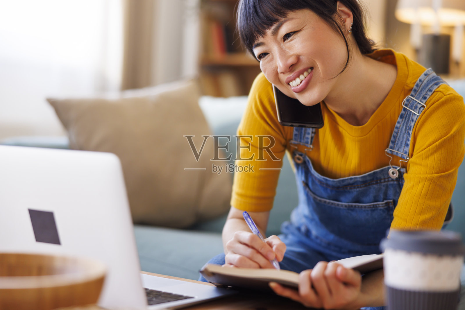 女性在家工作,一边在记事本上写笔记,一边参加在线会议照片摄影图片