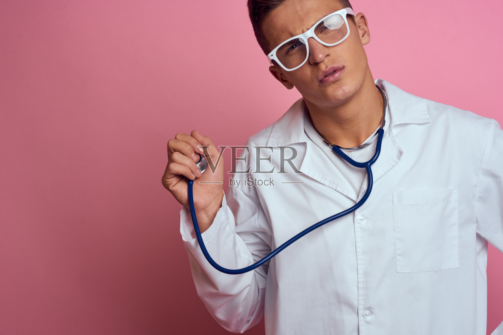男医生身穿医疗服,脖子上挂着听诊器,背景是粉红色的,脸上戴着眼镜照片摄影图片
