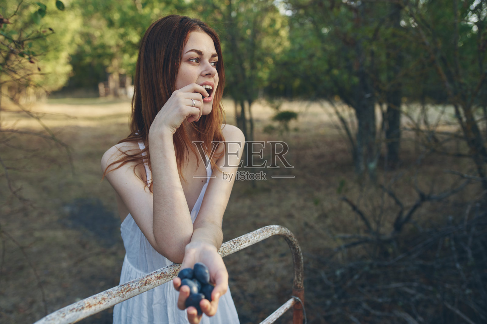 一个快乐的女人抱着一串葡萄,靠在花园外面的铁床上照片摄影图片