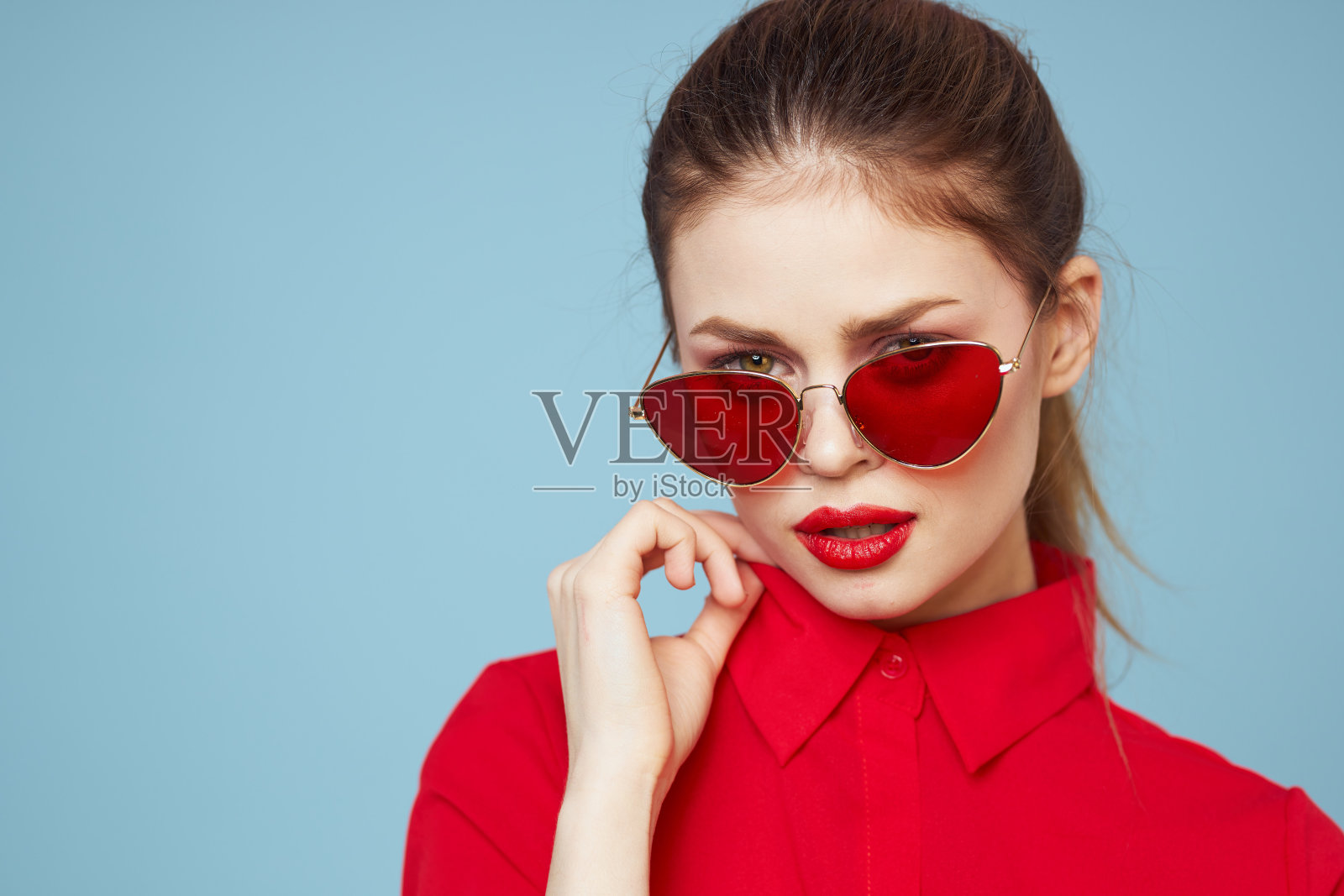 可爱的女人戴着墨镜,明亮的妆容,红唇,迷人的蓝色背景照片摄影图片