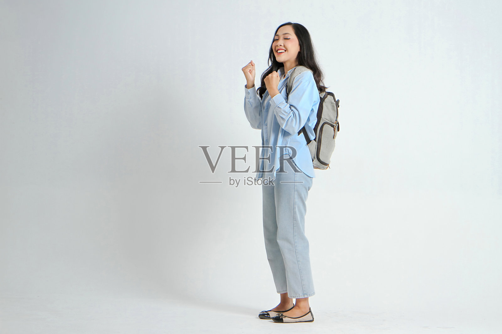 一个快乐的亚洲印尼女人的背光照,她穿着休闲装,背着背包,背景是孤立的照片摄影图片