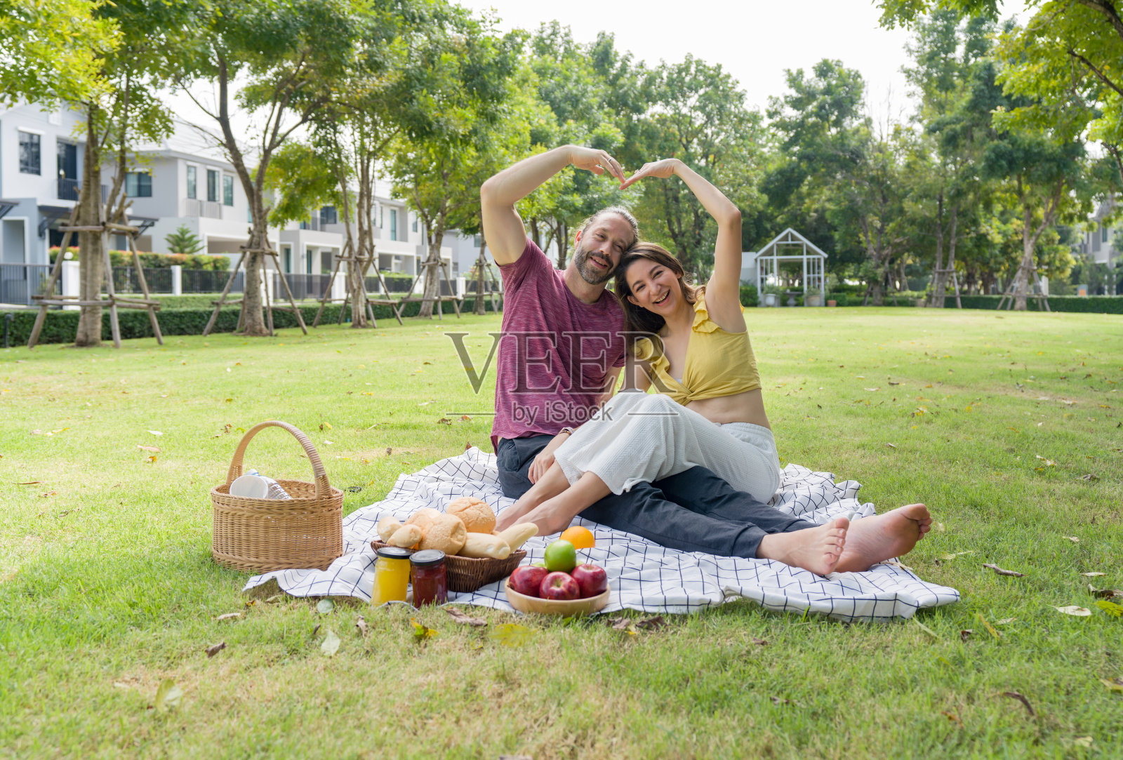 在风景优美的公园里,一对情侣坐在草地上,用手做成心形,表达爱意。照片摄影图片