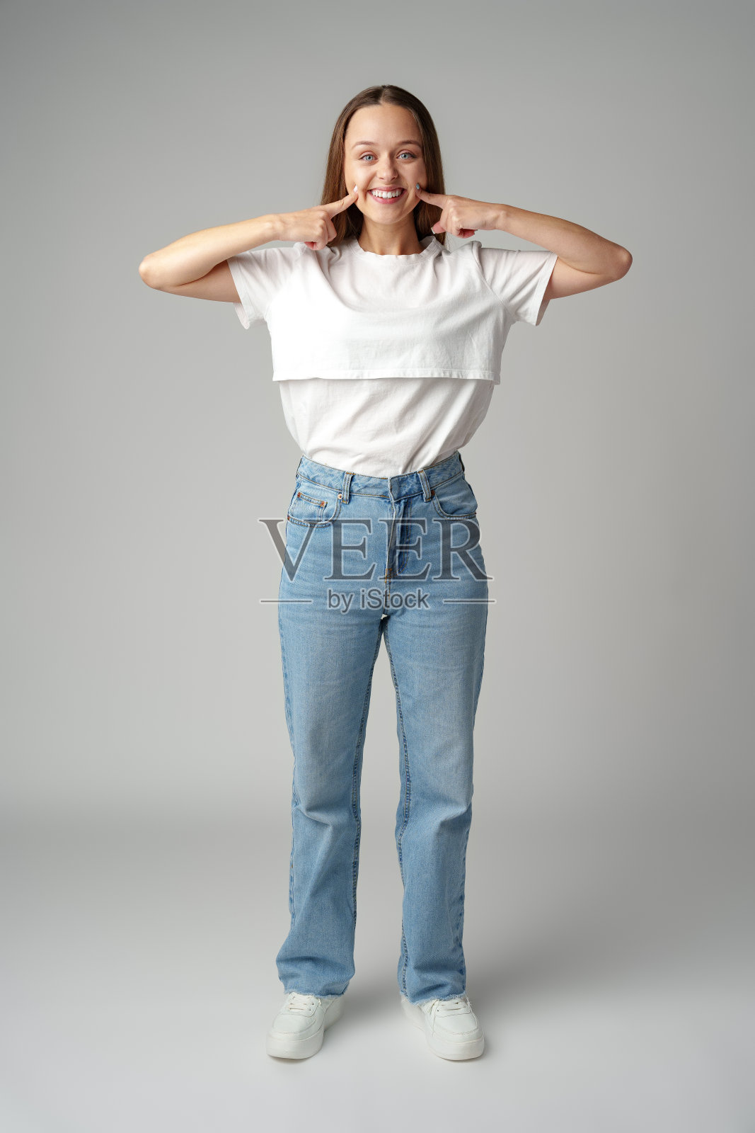 照片上美丽的年轻女子微笑着指着灰色背景上的牙齿照片摄影图片