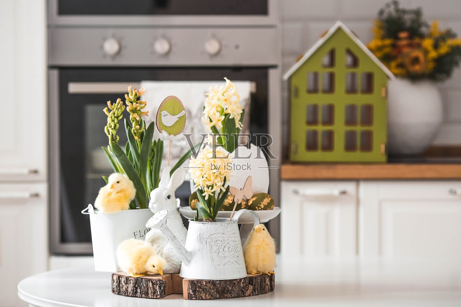 复活节快乐。春天黄色的风信子花插在鸡蛋形的花瓶里,小鸡放在白色的桌子上。背景是一间白色的斯堪的纳维亚风格厨房。房子里的复活节装饰。照片摄影图片